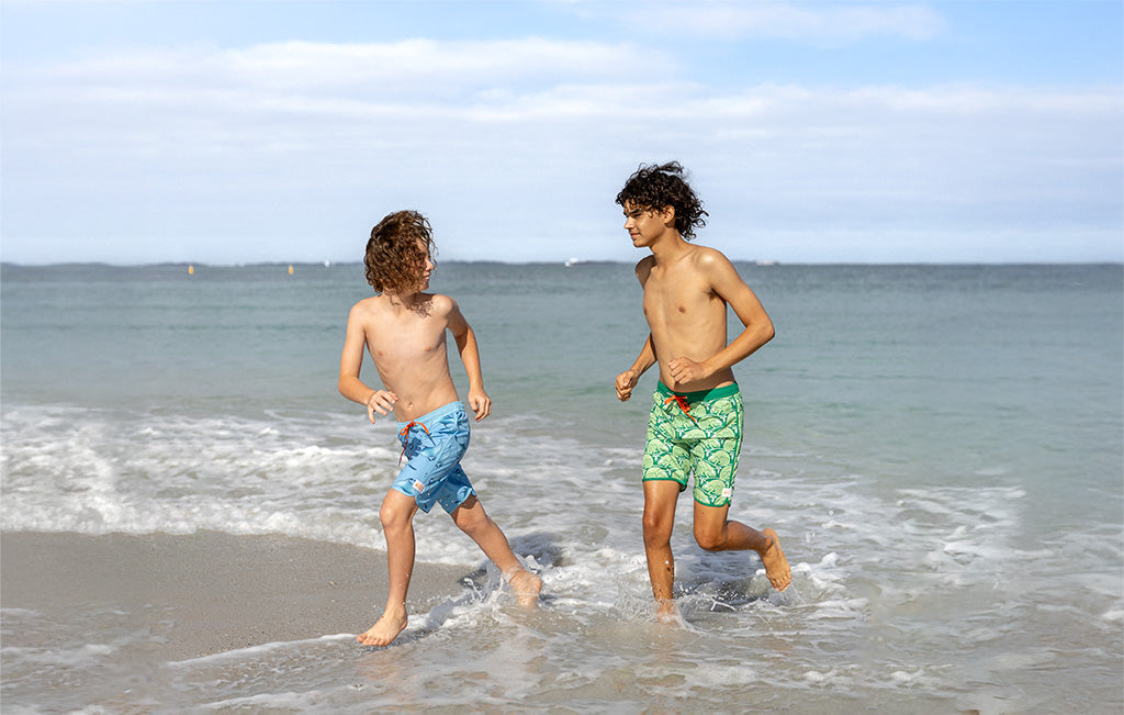 KIDS Sustainable Boardies Rashies Beachwear Collection made from Recycled Plastic Bottles by South Beach Boardies. A boy and a teenager in colourful shorts run along South Beach Fremantle