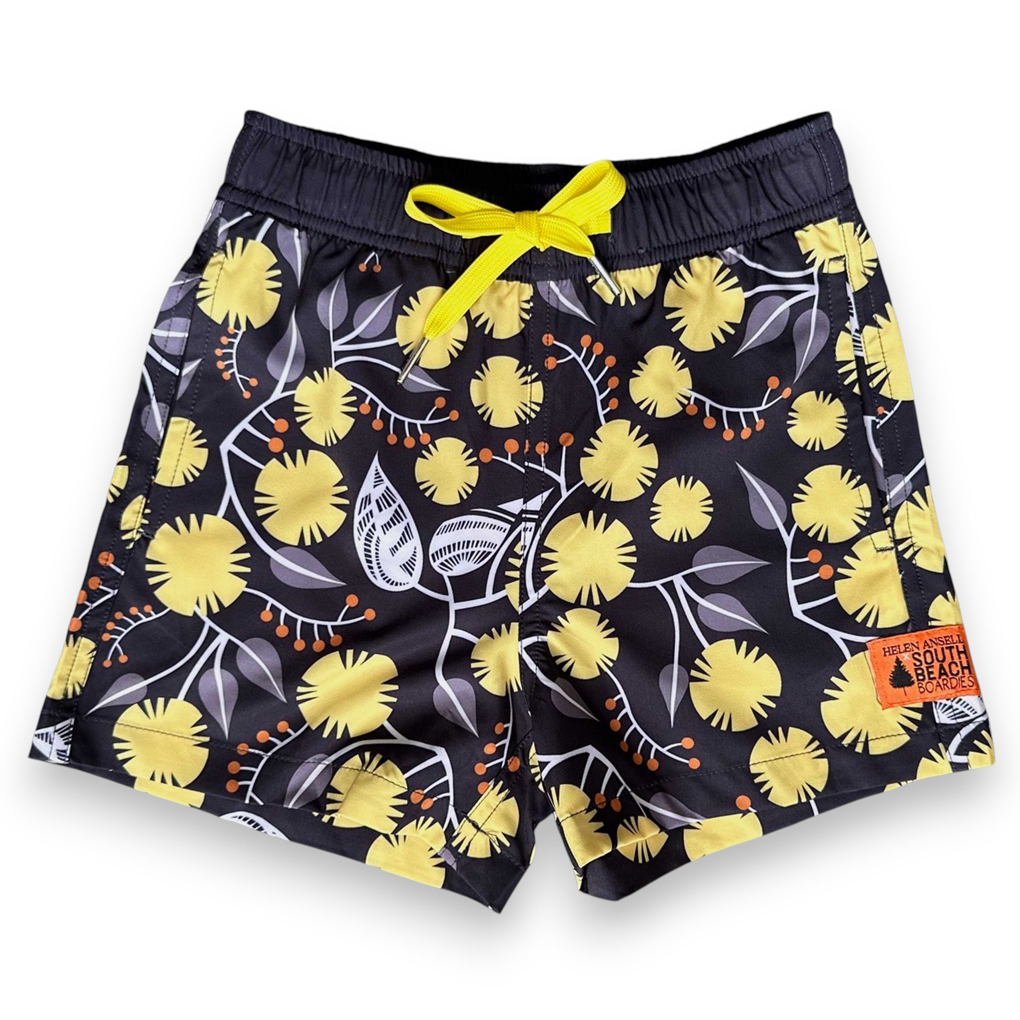 West Australian wattle patterned shorts with yellow flowers and grey leaves on a dark background, by South Beach Boardies x Helen Ansell, front view