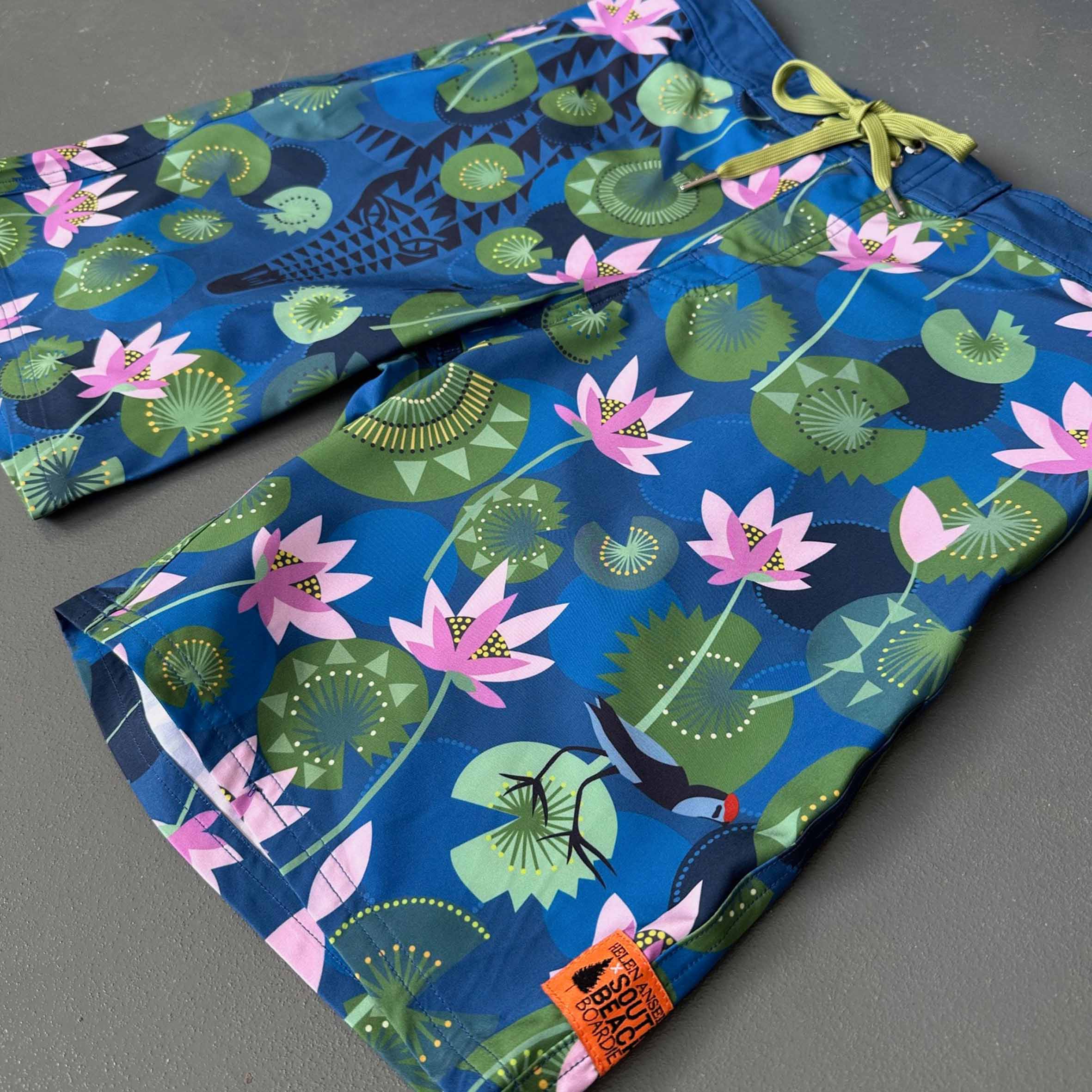 Blue swim shorts with hidden crocodile pink floral and green leaf pattern , made from recycled plastic bottles by South Beach Boardies x Helen Ansell