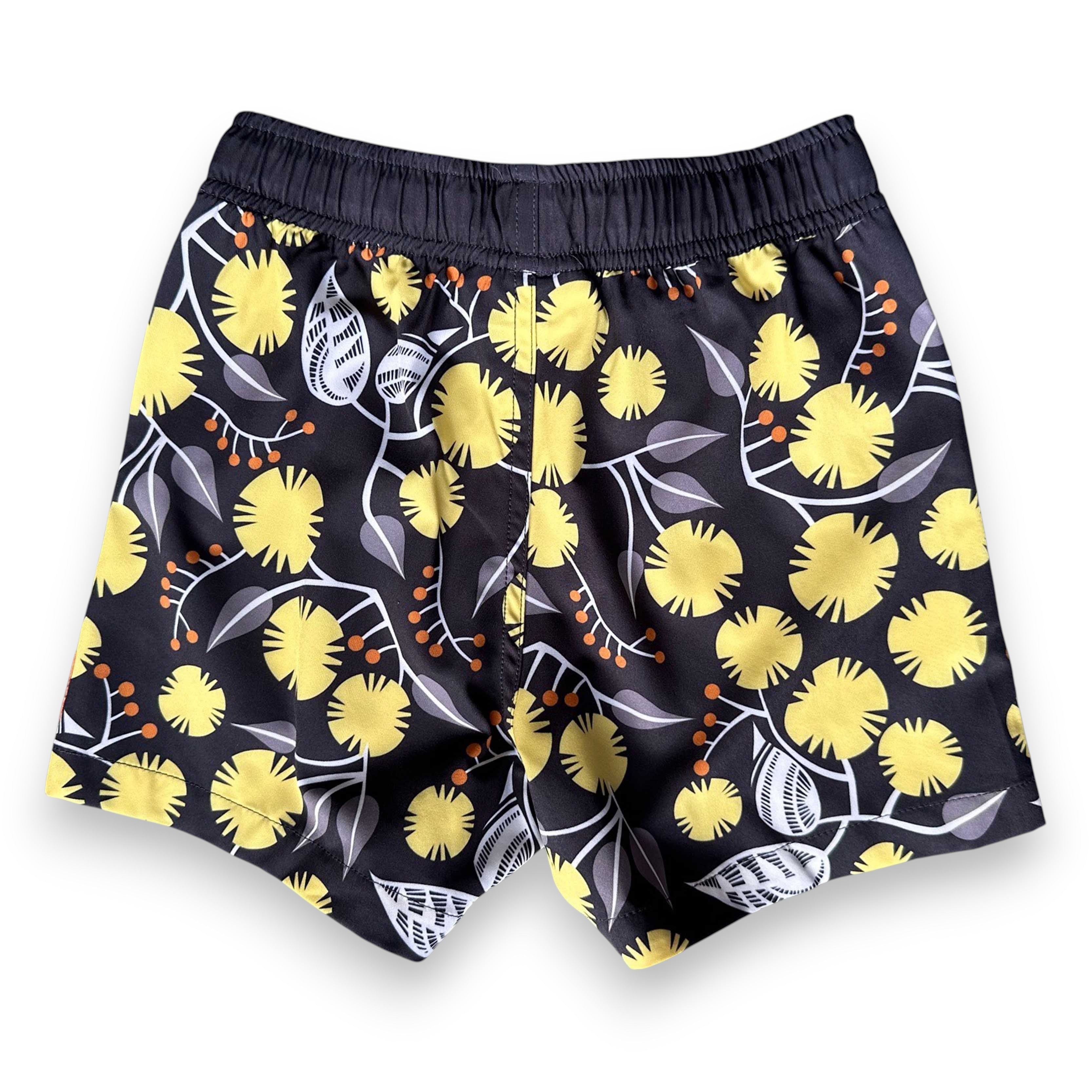 West Australian wattle patterned kids swim shorts with yellow flowers and grey leaves on a dark background, by South Beach Boardies x Helen Ansell, back view