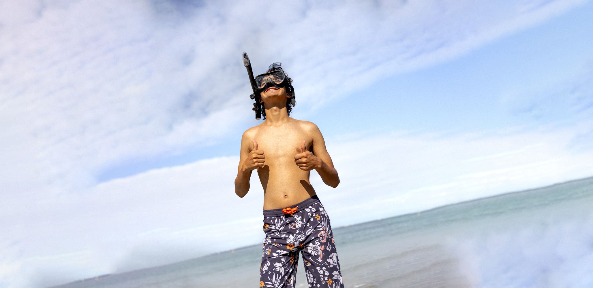 Teenage boy wearing snorkeling gear on a beach with a cloudy sky. South Beach Boardies Kids Long Length Boardshorts made from recycled plastic bottles by South Beach Boardies