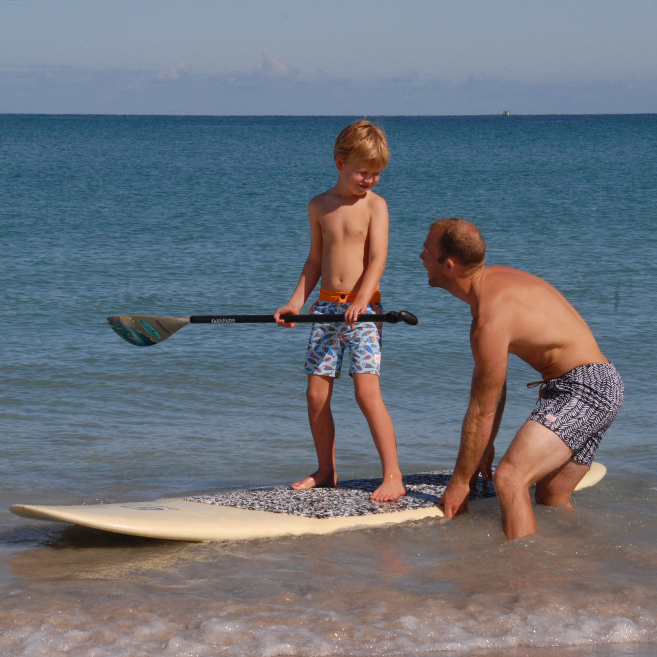 Boy learns to paddleboard wearing SBB Kids Going Out Boardies in Hooray for Fish!